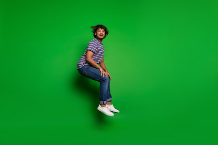 Portrait photo of young indian funny active positive man student jumping in striped t shirt and...