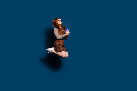 Full length photo of funky pretty lady dressed plaid outfit jumping enjoying beverage emtpy space isolated dark blue color backgroundの写真素材