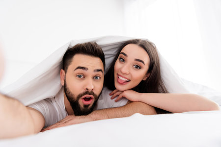 Photo of carefree funky couple wear white t-shirts recording video stick out indoors apartment bedroomの写真素材