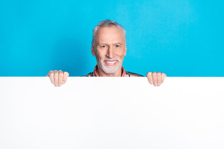 Photo of glad nice senior man wear striped stylish clothes hands hold empty space isolated on blue...