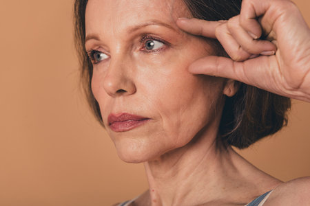 No filter close up photo of lovely adorable senior woman lifting effect cream isolated on beige color backgroundの写真素材