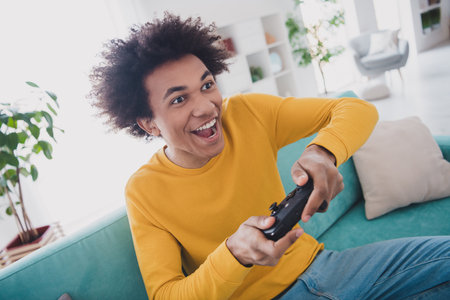 Photo of positive cheerful man sitting divan playing video game cool weekend rest relax living room indoorsの写真素材