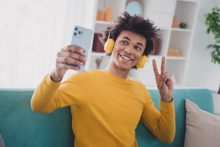 Portrait of nice young man phone make selfie v-sign wear yellow pullover white interior flat indoors