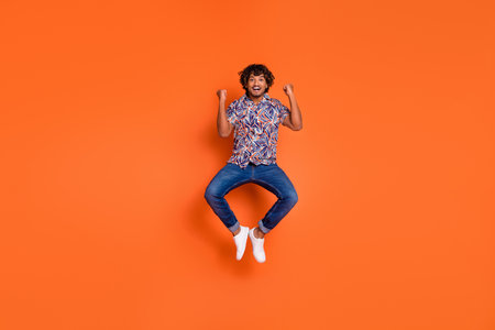 Full length photo of handsome young man jump raise fists dressed stylish colorful garment isolated...