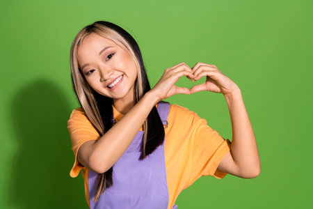 Photo portrait of lovely young lady heart gesture dressed stylish violet yellow garment isolated on green color backgroundの写真素材
