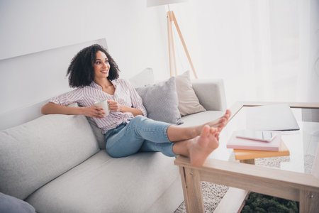 Photo of dreamy charming nice woman sitting on sofa enjoying cozy moment white light interior living room indoorsの写真素材