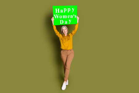 Full length photo of charming positive woman wear shirt rising 8 march placard empty space isolated khaki color backgroundの写真素材
