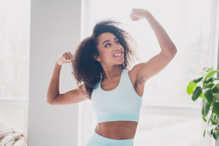 Portrait of pretty sportive young girl arms show flex biceps sportswear morning workout apartment...