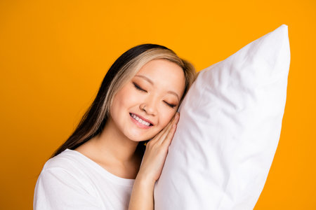 Photo of cute charming dreamy woman wear white trendy nightwear soft pillow isolated on yellow color backgroundの写真素材