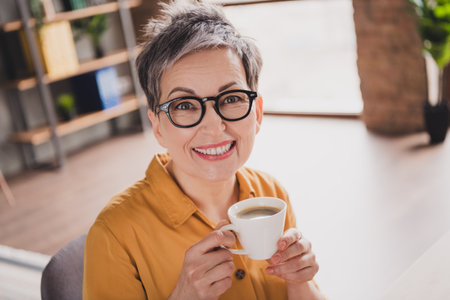 Photo of pretty retired woman drink coffee beverage dressed yellow formalwear modern workplace...