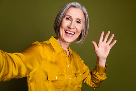 Photo of adorable positive woman wear shirt waving arm hi recording video vlog isolated khaki color...