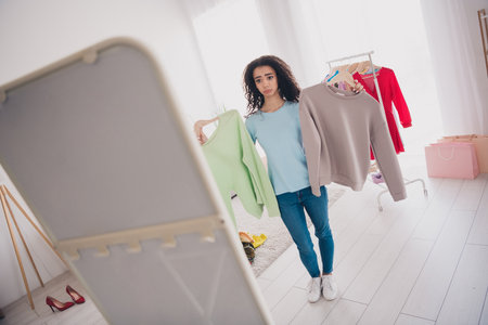 Portrait of pretty young girl hands hold clothes hanger look decide mirror apartment indoorsの写真素材