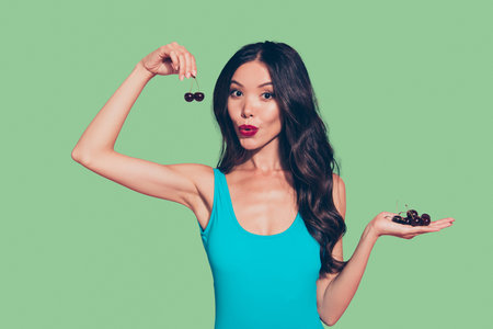 Portrait of nice amazed wondered cute sweet lovely winsome attractive wavy-haired girl red lips holding in hands ripe cherries isolated over pink pastel backgroundの写真素材