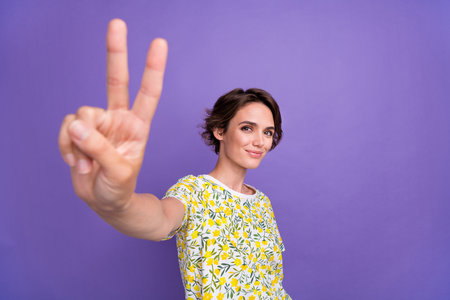 Portrait of pretty young woman demonstrate v-sign wear t-shirt isolated on purple color backgroundの写真素材