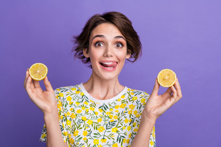Portrait of pretty young woman lick teeth hold juicy lemon wear t-shirt isolated on purple color...