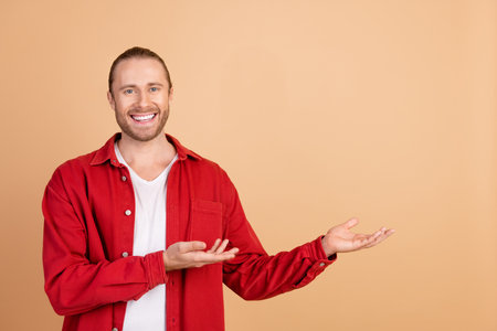 Photo of nice young man hands show empty space wear red shirt isolated on beige color backgroundの写真素材