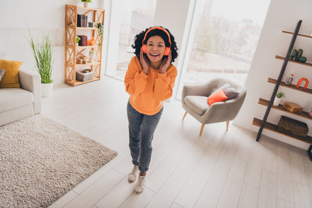 Photo portrait of lovely young lady earphones dance weekend dressed casual orange clothes cozy day light home interior living roomの写真素材