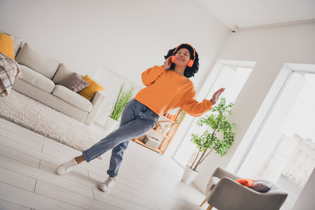 Photo portrait of lovely young lady dancing earphones dressed casual orange clothes cozy day light home interior living roomの写真素材