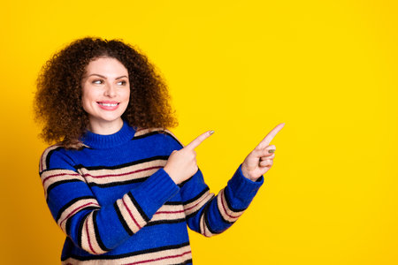 Portrait of adorable girl with wavy hairstyle wear knit pullover look directing at sale empty space isolated on yellow color backgroundの写真素材