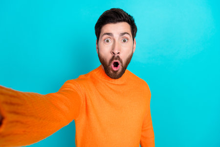 Photo of shocked nice young man wear orange trendy clothes make selfie isolated on cyan color backgroundの写真素材