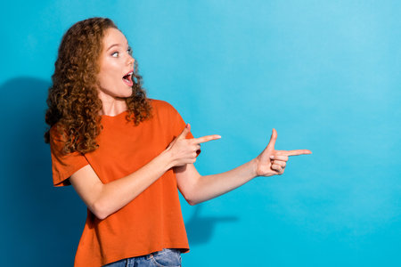 Photo of young funny promoter red hair lady wearing orange t shirt directing fingers empty blank cheap price product isolated on blue color backgroundの写真素材