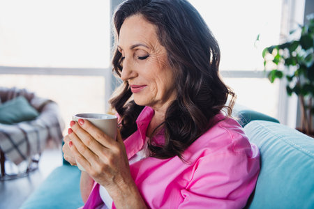 Photo of cute charming retired woman enjoying weekend drinking fresh hot tea cappuccino indoorsの写真素材