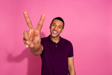 Photo portrait of nice young male show v-sign dressed stylish violet garment isolated on pink color backgroundの写真素材