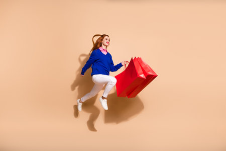 Full length portrait of pretty young lady shop bags jump run empty space wear sweater isolated on beige color backgroundの写真素材