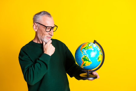Photo portrait of nice senior man look thoughtful globe dressed stylish green clothes isolated on yellow color backgroundの写真素材