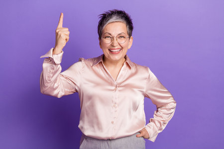 Photo portrait of nice pensioner female point up eureka empty space wear trendy satin outfit isolated on violet color backgroundの写真素材