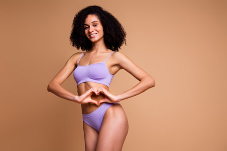 Unretouched photo of pretty model girl show heart symbol isolated on beige color backgroundの写真素材