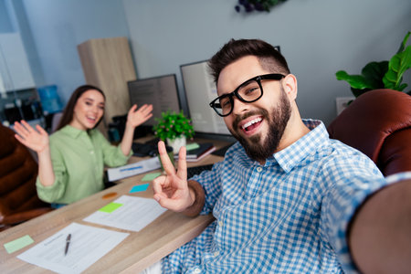 Photo of cheerful smiling colleagues formalwear tacking selfie showing v-sign indoors workplace workshopの写真素材
