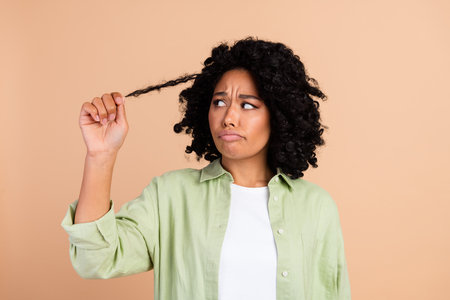 Portrait of pretty young woman hold hair curl wear green shirt isolated on beige color backgroundの写真素材