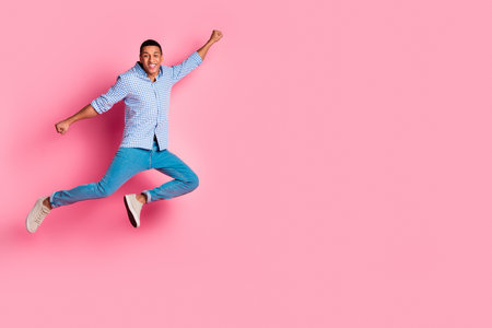 Full length photo of handsome carefree guy wear plaid shirt jumping high hurrying emtpy space isolated pink color backgroundの写真素材