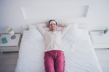 Photo of happy dreamy man enjoying lying in soft comfortable cosy bedrooom bed white interior insideの写真素材