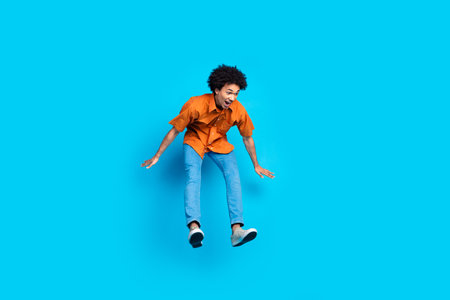 Full length photo of shocked funny guy wear orange shirt jumping high emtpy space isolated blue...