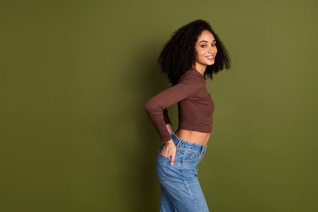 Photo portrait of pretty young girl touch back pockets jeans wear trendy brown outfit isolated on khaki color backgroundの写真素材