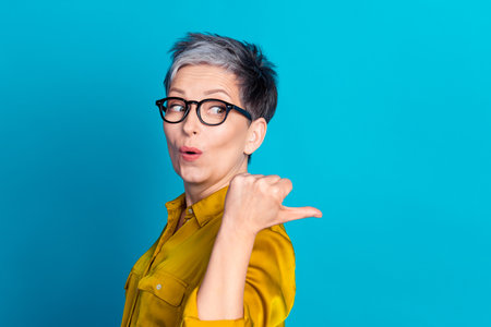 Photo of confident impressed lady dressed shirt glasses pointing thumb emtpy space isolated blue color backgroundの写真素材