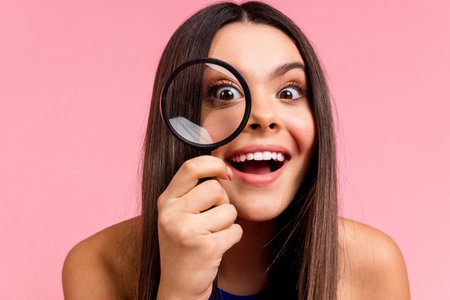 Photo of charming excited girl smiling looking you enlarging glass isolated pink color background