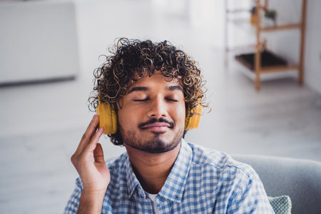 Photo of dreamy good mood man wear checkered shirt staying home listening songs earphones indoors house apartment roomの写真素材