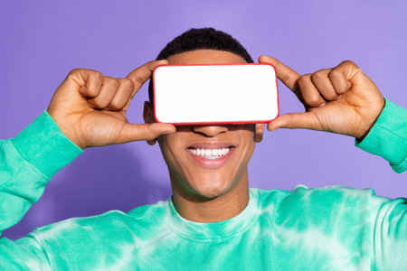 Photo of cheerful positive guy dressed turquoise sweatshirt modern device cover eyes emtpy space...