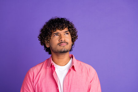 Photo of nice young man look interested empty space wear pink shirt isolated on violet color backgroundの写真素材