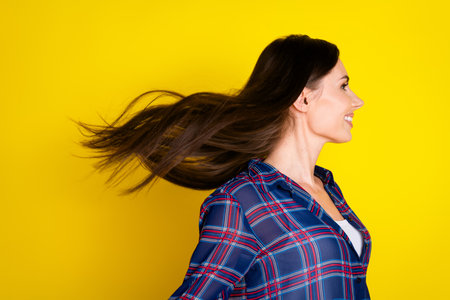 Photo portrait of attractive young woman fluttering hair shampoo dressed stylish plaid clothes isolated on yellow color backgroundの写真素材
