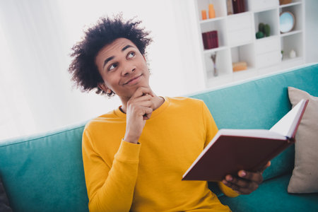 Portrait of nice young man hold book contemplate wear yellow pullover white interior flat indoors