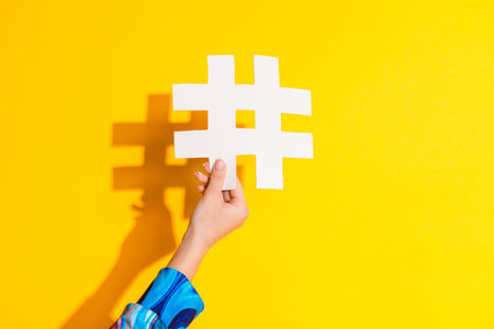 Cropped photo of lady hand hold white hashtag dressed stylish colorful garment isolated on yellow color backgroundの写真素材