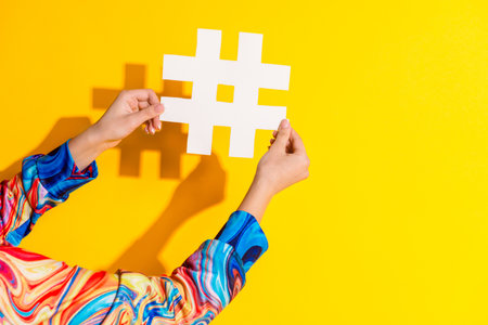 Cropped photo of woman hands hold hashtags dressed stylish colorful clothes isolated on yellow color...