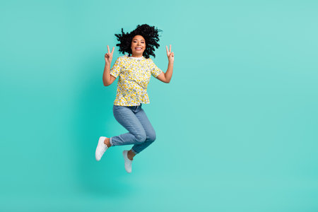 Full size photo of nice young woman jump v-sign empty space wear t-shirt isolated on teal color...