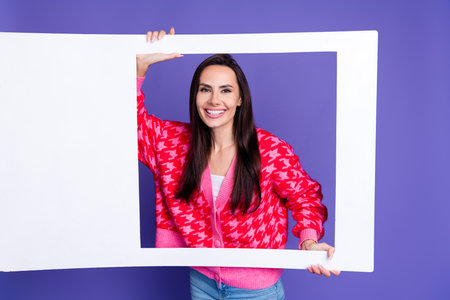 Photo of cute pretty lady dressed pink cardigan holding paper photo frame empty space isolated violet color backgroundの写真素材