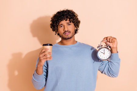 Portrait of overwhelmed sad middle eastern guy dressed blue pullover hold cappuccino alarm in arm...