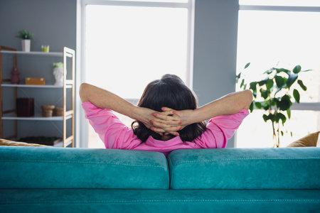 Photo portrait of attractive retired woman sit sofa hands behind head relax dressed stylish pink clothes cozy interior home living roomの写真素材